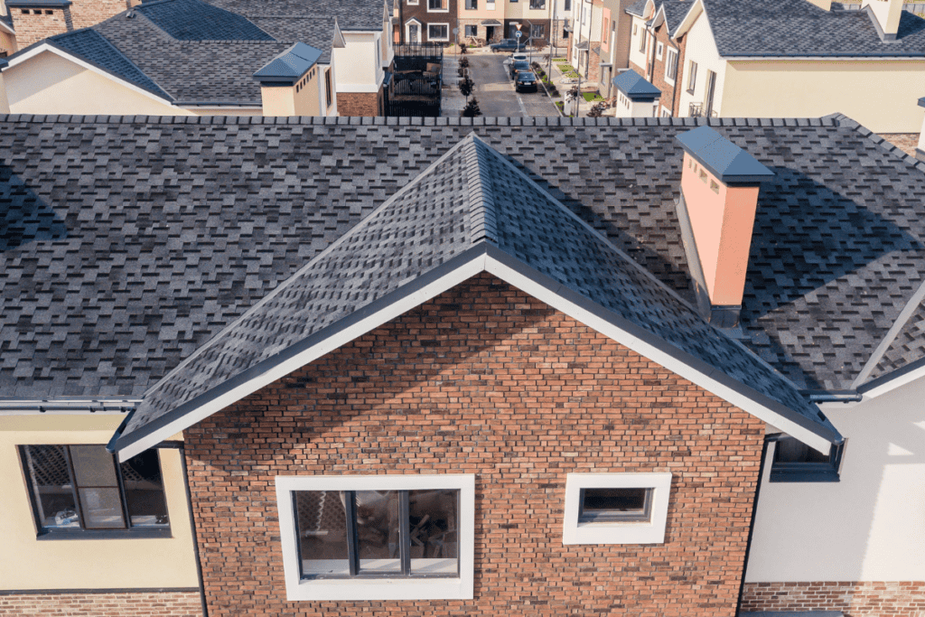 Aerial view of a suburban neighborhood showing a brick house with a dark gray shingled roof and surrounding homes.