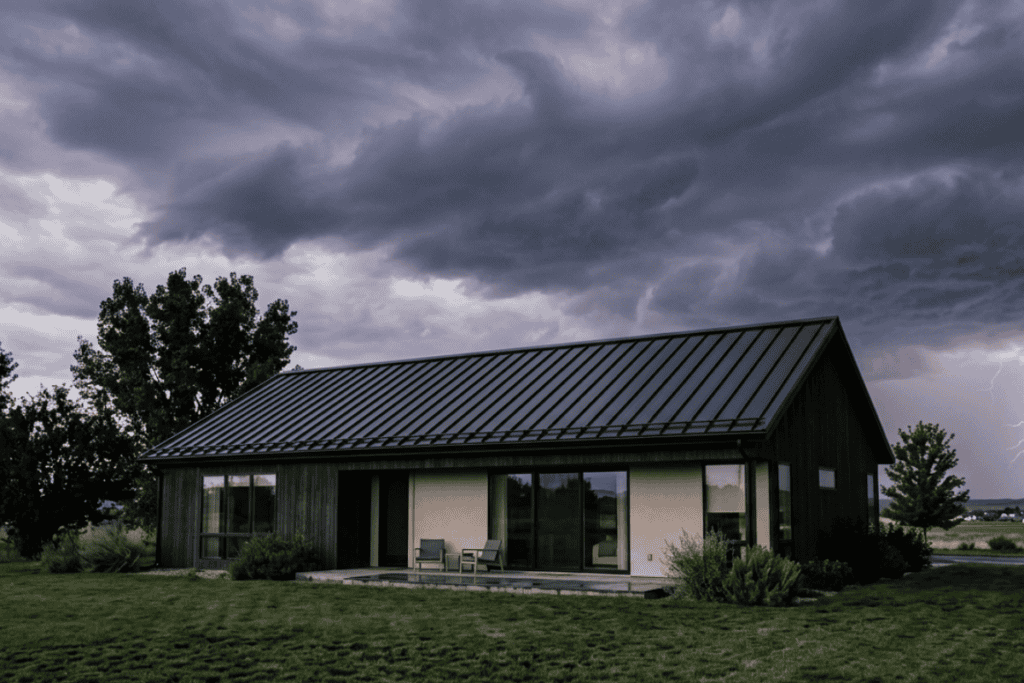 Stormy sky over a modern single-story house with a metal roof and small patio seating area.