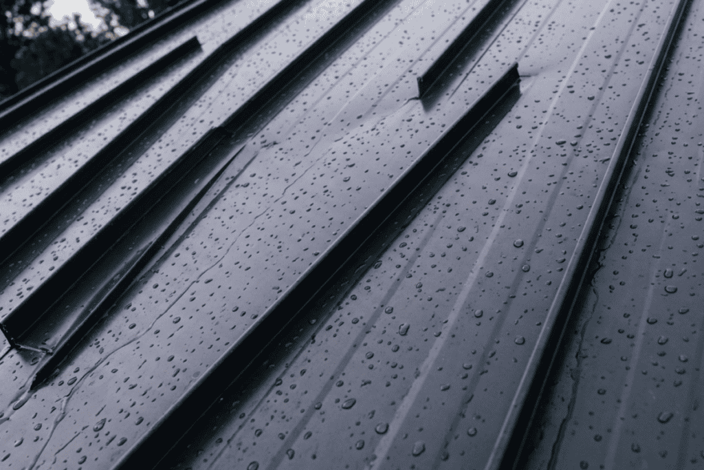 what-happens-if-lightning-hits-a-metal-roof - Tulsa Roofing | Standard Exteriors & Roofing Rain droplets on corrugated metal roof panels with diagonal seams and reflections.